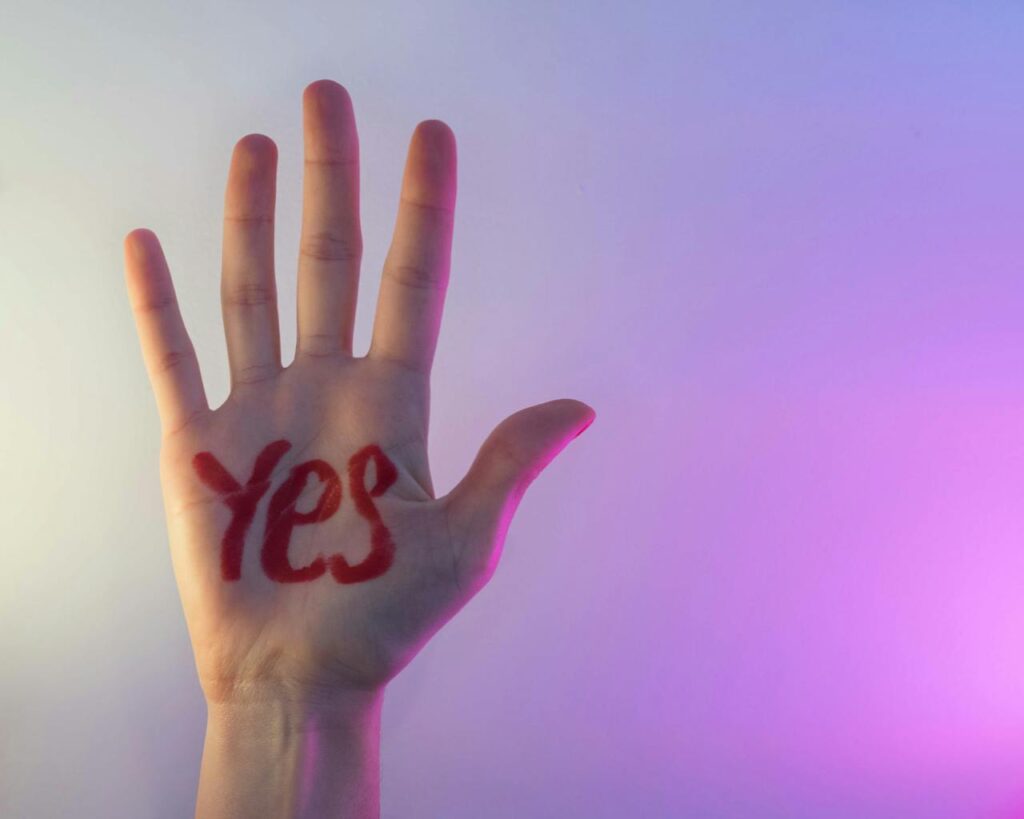 Close-up of a hand with 'YES' written on the palm against a colorful gradient backdrop.