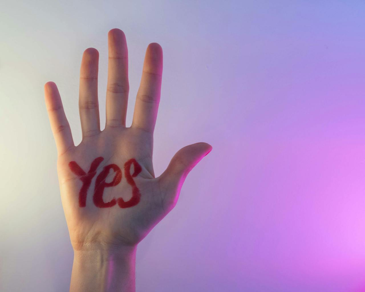 Close-up of a hand with 'YES' written on the palm against a colorful gradient backdrop.